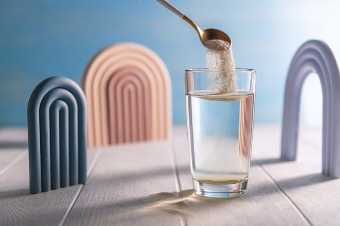 A spoon pours ORS powder into a glass of water, displayed with minimalist arch decorations against a light blue background