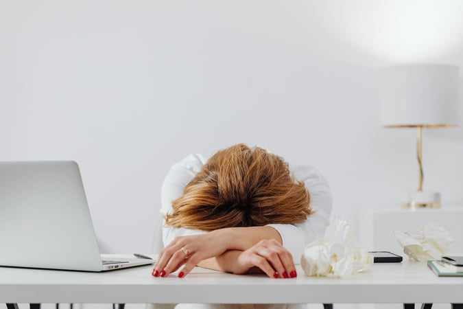 Tired woman resting her head on her arms at a desk with a laptop
