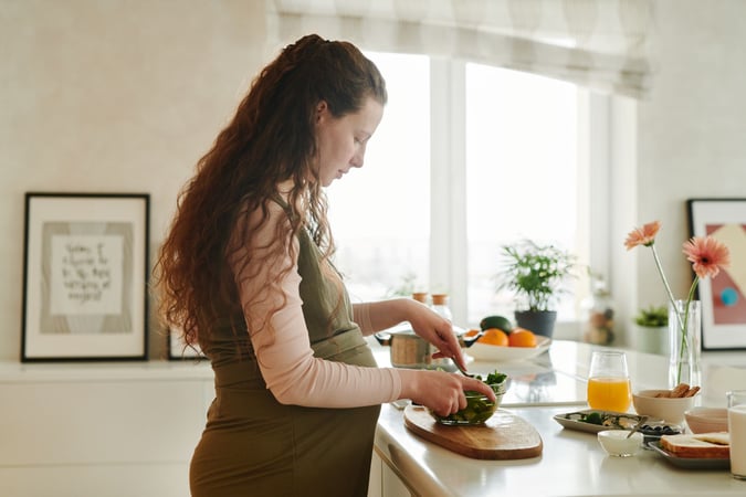 Pregnant woman with curly hair prepares a meal on a kitchen counter