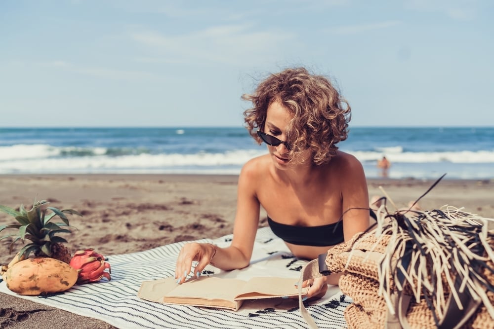 Confident woman with glowing skin reading at the beach