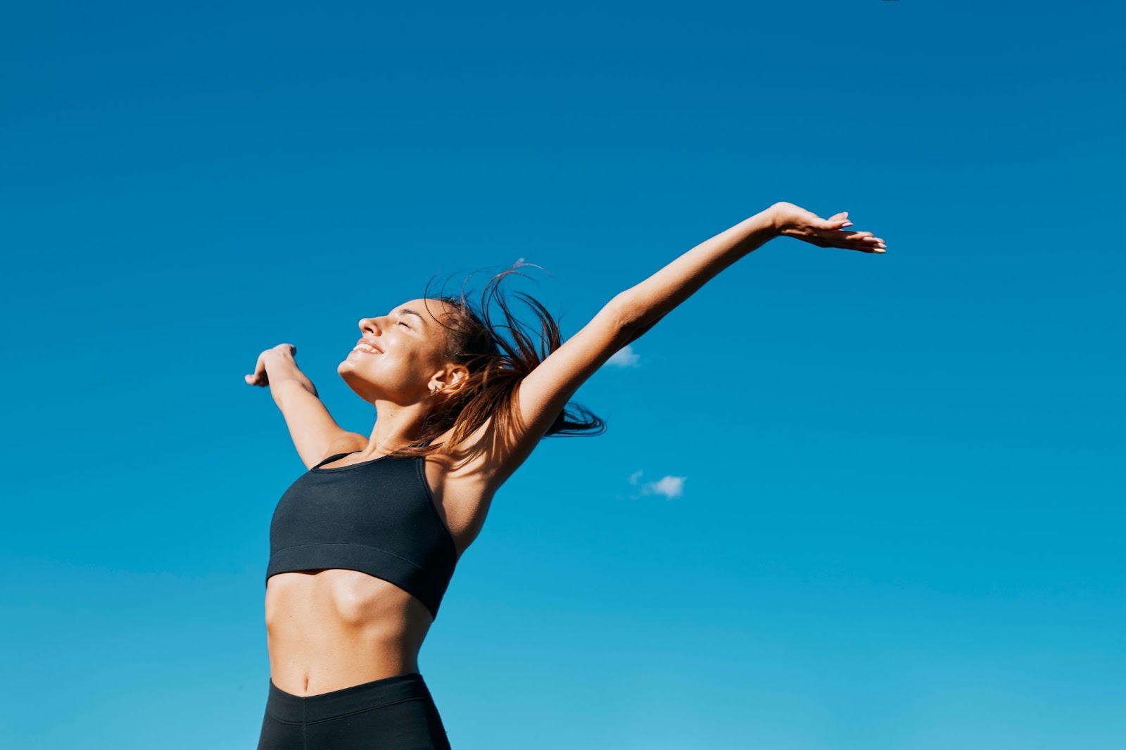 Young woman with her arms outstretched outside on a beautiful day, clear blue skies.