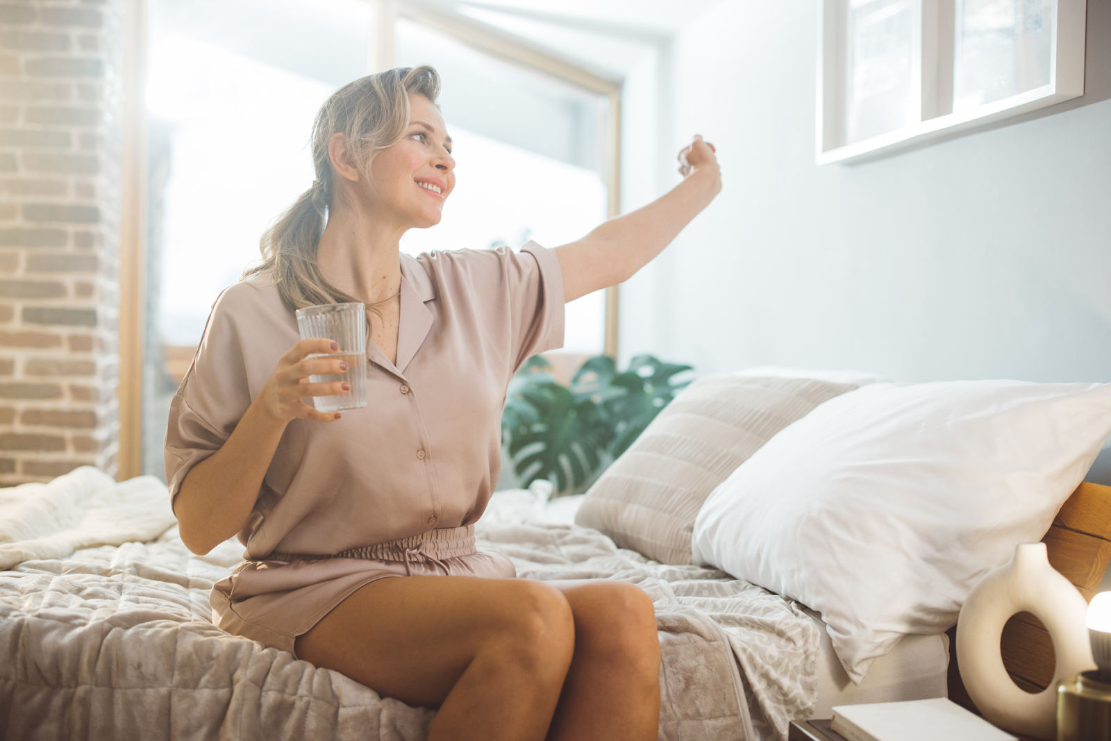 A woman sitting in bed holding a glass of water, waking up feeling refreshed after an IV therapy session