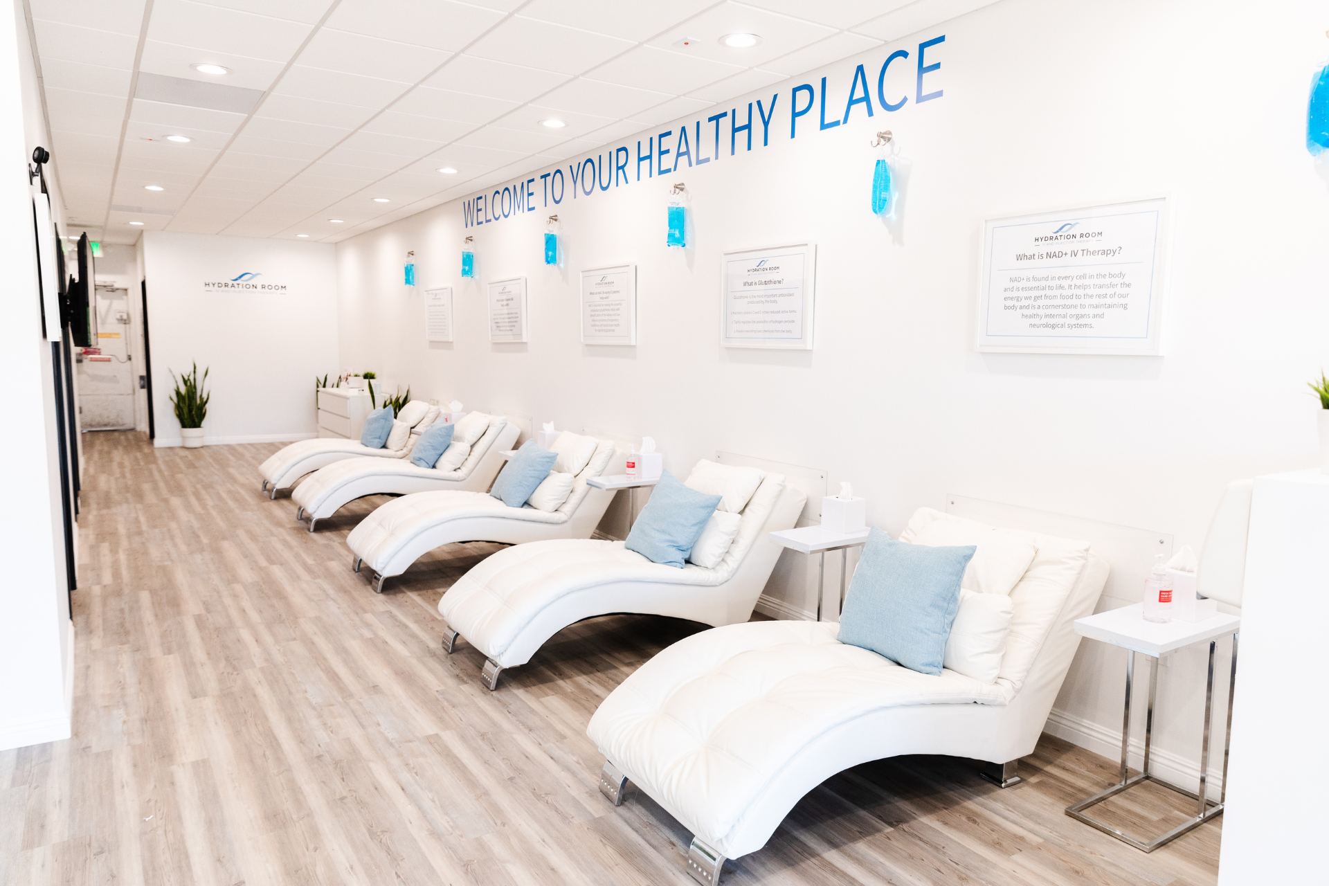 A bright, modern IV hydration clinic with a row of white reclining lounge chairs lined along the wall