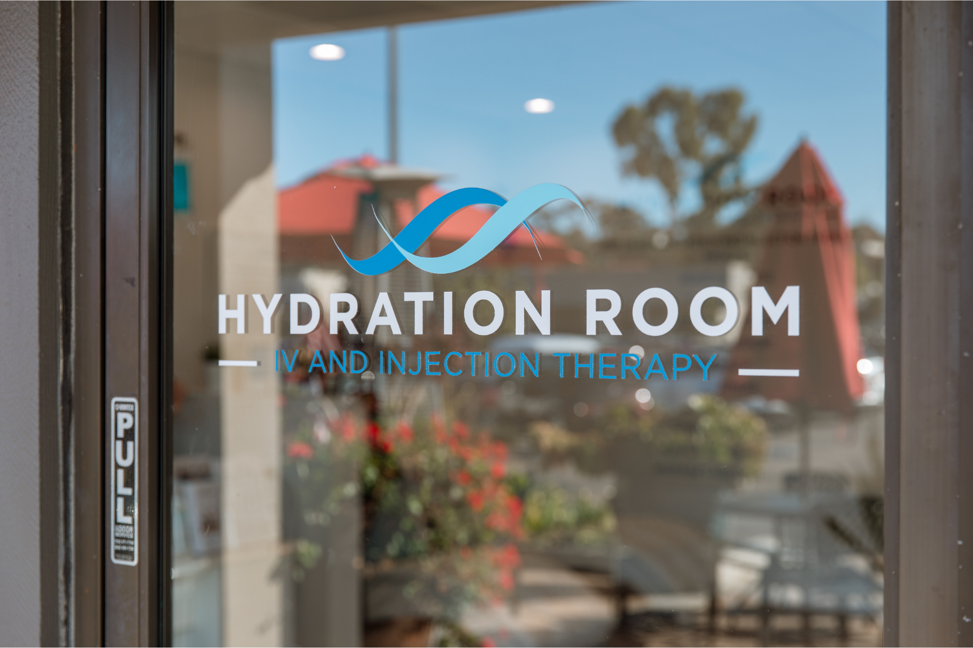Glass entrance door with the “Hydration Room – IV and Injection Therapy” logo in white and blue lettering