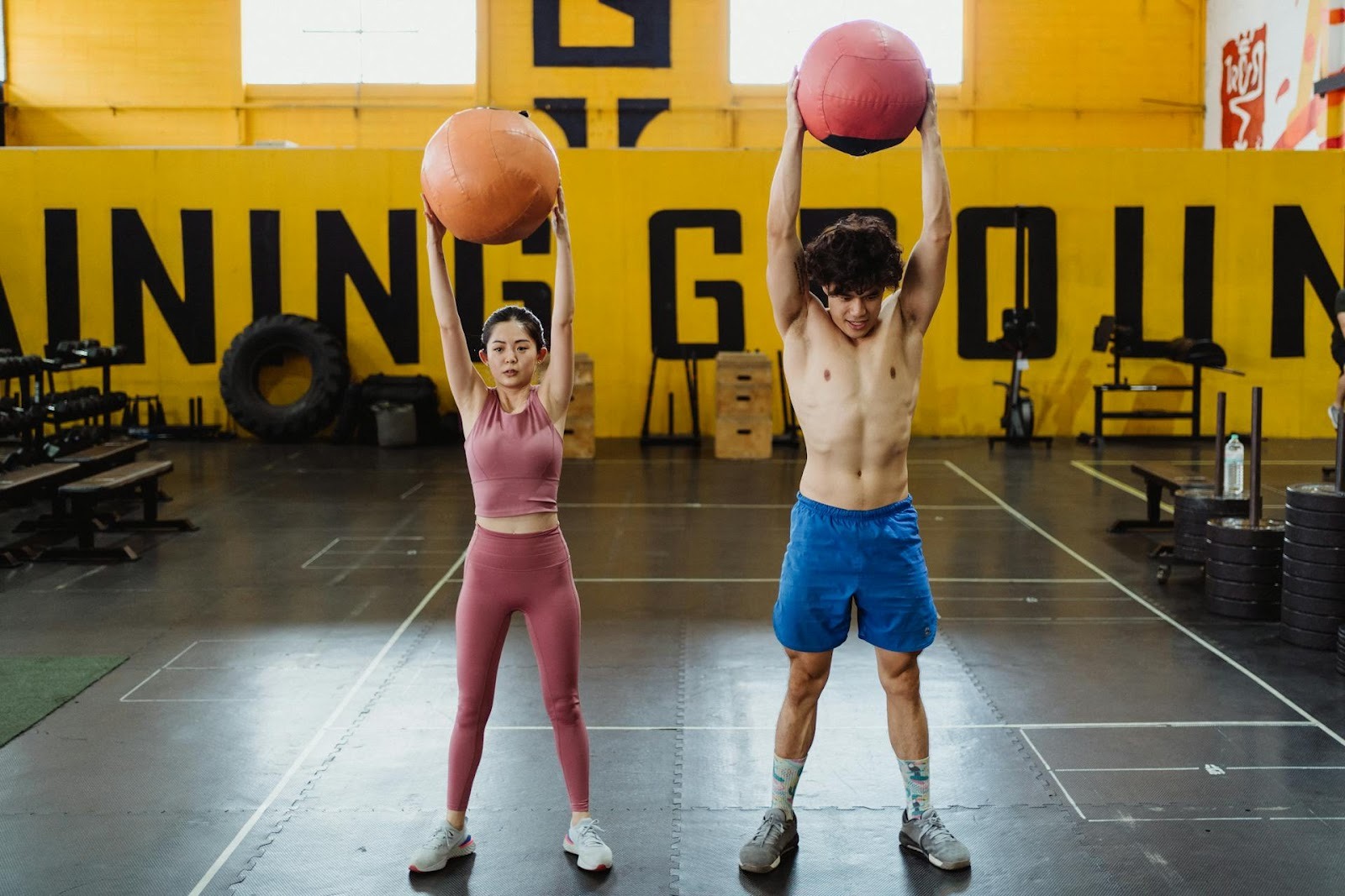 A man and a woman performing overhead medicine ball holds in a gym