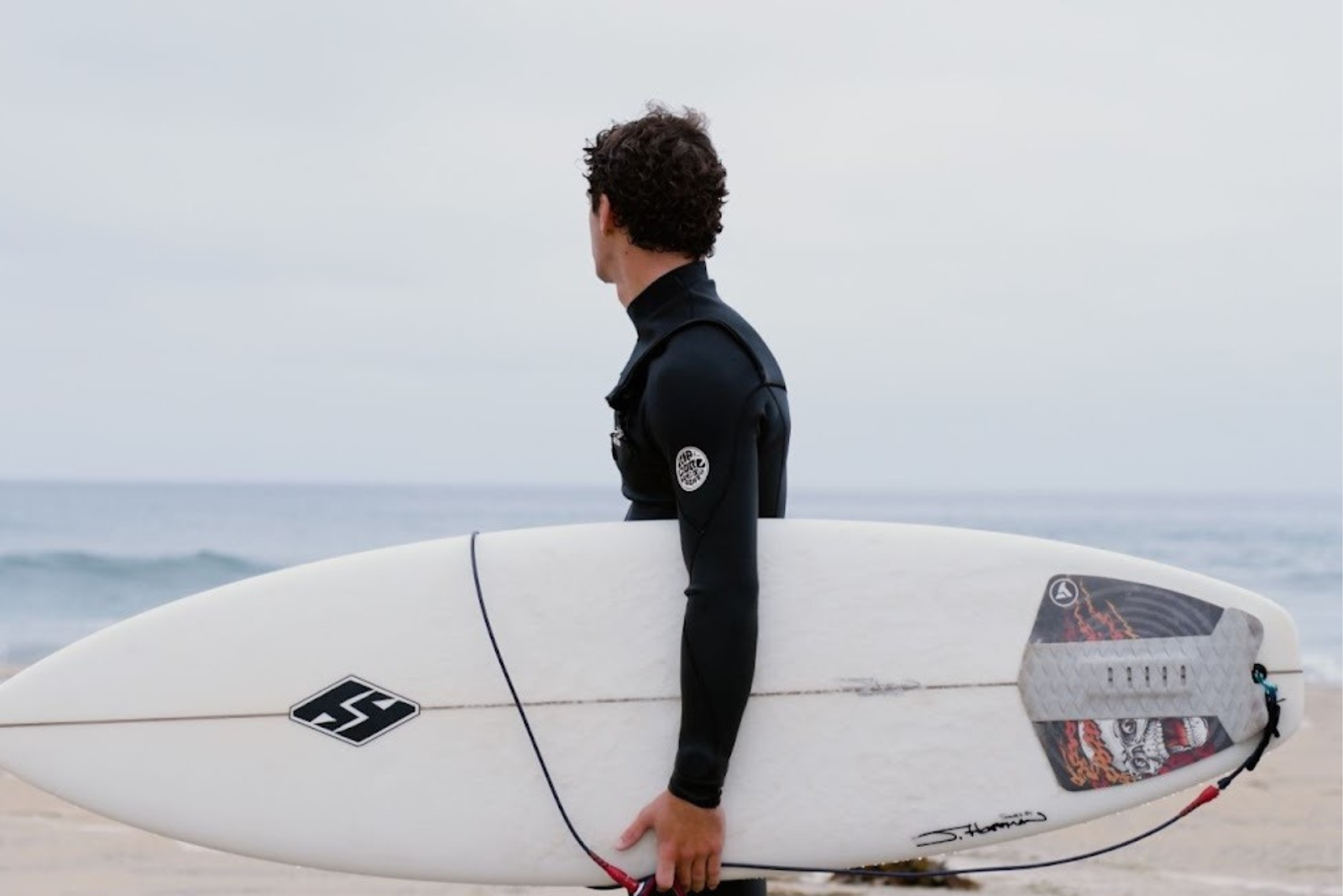 A man holding a white surfboard as he walks the shoreline.