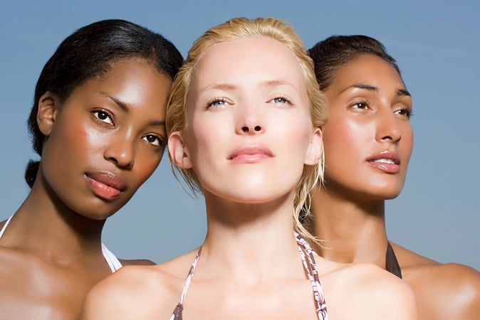 Three women pose facing the camera, skin glowing.