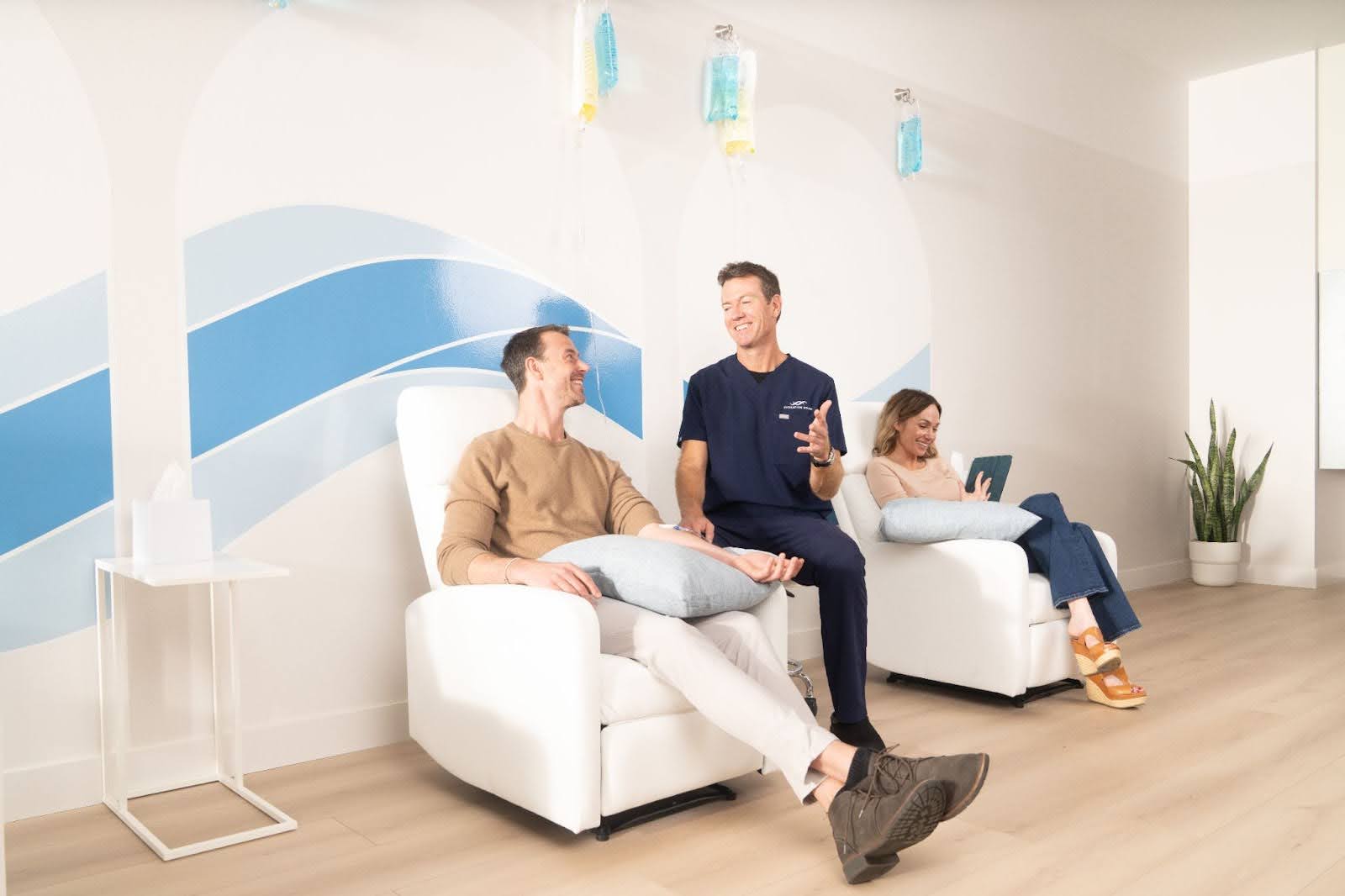 Dr. Florie talks about IV health and wellness with a patient at a Hydration Room while another patient sits in a chair behind him. 